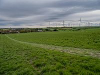 a green field with windmills in the distance under a cloudy sky with white clouds