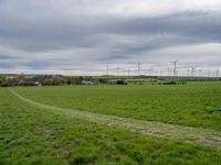 a green field with windmills in the distance under a cloudy sky with white clouds