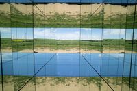 two pictures of a field with a body of water in it and the sky reflected by glass windows