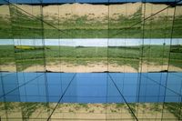 two pictures of a field with a body of water in it and the sky reflected by glass windows