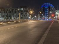 a picture of a street near some buildings lit up blue at night from the sidewalk