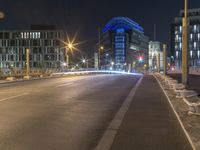 a picture of a street near some buildings lit up blue at night from the sidewalk