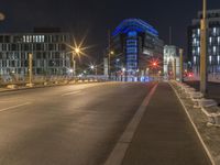 a picture of a street near some buildings lit up blue at night from the sidewalk