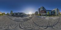 a fish eye image of three large buildings and a courtyard in the foreground with cobblestones all around