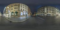 an intersection with traffic passing by and buildings lit up at night in front of them