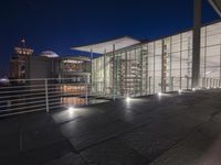 a glass walkway leading to a large building near a bridge with buildings in the background