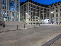 an empty courtyard at night with steps going up to it and other buildings in the background