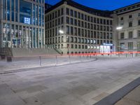 an empty courtyard at night with steps going up to it and other buildings in the background