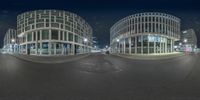 two buildings in the middle of a street at night with some lights on and a car passing by