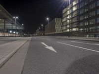 a street with white lines in an empty lot at night with buildings and cars parked on both sides
