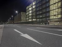 a street with white lines in an empty lot at night with buildings and cars parked on both sides