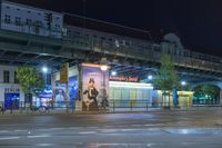 a person walking on a street next to a billboard under a road bridge at night