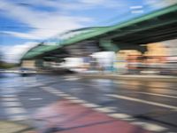 traffic lights on an empty street with blurred buildings behind it and a bridge above it