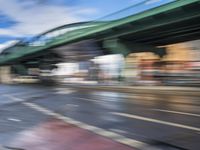 traffic lights on an empty street with blurred buildings behind it and a bridge above it