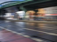 traffic lights on an empty street with blurred buildings behind it and a bridge above it