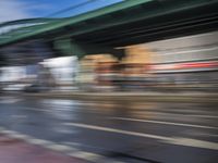 traffic lights on an empty street with blurred buildings behind it and a bridge above it