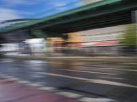 traffic lights on an empty street with blurred buildings behind it and a bridge above it