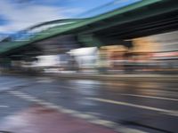 traffic lights on an empty street with blurred buildings behind it and a bridge above it