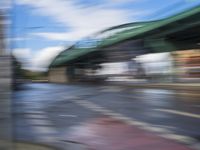 traffic lights on an empty street with blurred buildings behind it and a bridge above it