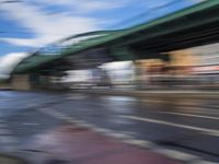 traffic lights on an empty street with blurred buildings behind it and a bridge above it