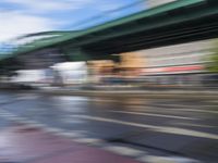 traffic lights on an empty street with blurred buildings behind it and a bridge above it