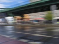 traffic lights on an empty street with blurred buildings behind it and a bridge above it