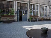 this is an old building with chairs and plants on it's patio table and two wooden benches