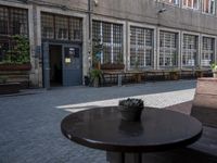 this is an old building with chairs and plants on it's patio table and two wooden benches