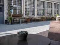 this is an old building with chairs and plants on it's patio table and two wooden benches