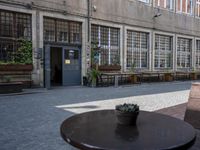 this is an old building with chairs and plants on it's patio table and two wooden benches