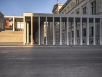 the large, empty sidewalk with multiple columns in front of the building with two signs