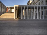 the large, empty sidewalk with multiple columns in front of the building with two signs