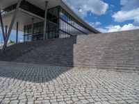 a person on a bike walking through a stone building entrance, in front of an enormous glass wall and stairs