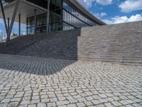 a person on a bike walking through a stone building entrance, in front of an enormous glass wall and stairs