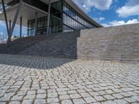 a person on a bike walking through a stone building entrance, in front of an enormous glass wall and stairs