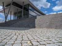 a person on a bike walking through a stone building entrance, in front of an enormous glass wall and stairs