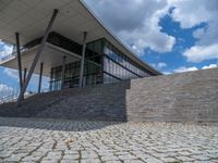 a person on a bike walking through a stone building entrance, in front of an enormous glass wall and stairs