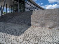 a person on a bike walking through a stone building entrance, in front of an enormous glass wall and stairs