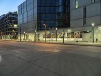 a paved street in the middle of buildings with tall windows at night, with car lights on