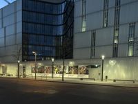 a paved street in the middle of buildings with tall windows at night, with car lights on