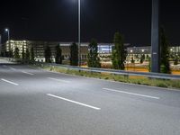 a highway that is empty near a building at night with lights on it and trees along one side