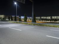 a highway that is empty near a building at night with lights on it and trees along one side