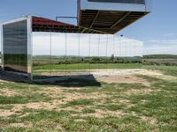 a building that is reflecting in the mirror glass at the entrance to a grassy area