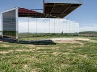 a building that is reflecting in the mirror glass at the entrance to a grassy area