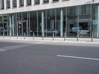 an empty city street next to a building and parked cars with double doors open on the side