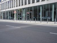 an empty city street next to a building and parked cars with double doors open on the side
