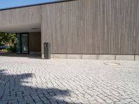 the empty walkway in front of a building has a small light post on it and two poles standing out against the wall