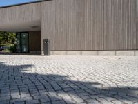 the empty walkway in front of a building has a small light post on it and two poles standing out against the wall