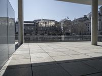 an empty concrete patio with white columns overlooking buildings and river in the middle of it