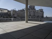 an empty concrete patio with white columns overlooking buildings and river in the middle of it